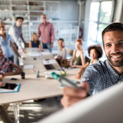 Happy businessman writing a business plan on whiteboard to his team on a meeting in board room.